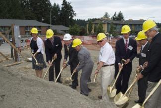 People in hardhats symbolically shoveling dirt at a property's groundbreaking ceremony