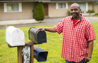 Man standing at mailbox in front of house and yard